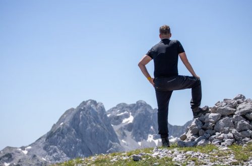 A hiker stands atop a rocky peak, enjoying a breathtaking mountain view on a clear day.